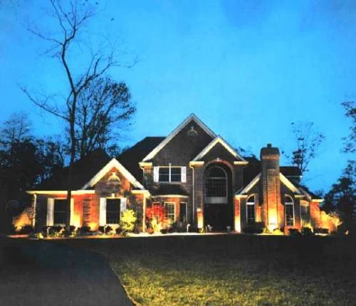 A large brick house lit at dusk against a deep blue sky.
