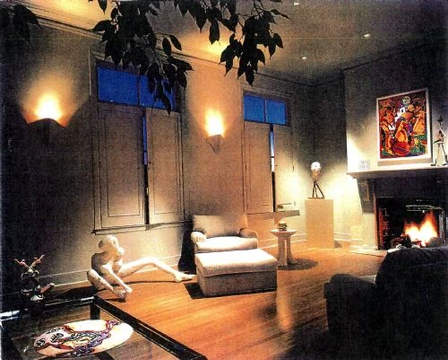 A living room in the evening with the fireplace lit and picture lights over the art.